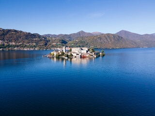 Obraz premium San Giulio Island within Lake Orta in Piedmont, Italy. aerial drone view in autumn. mountains, blue water and reflection