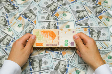 Hands Holding Argentinian Money Against $100 Bills Background. Economic Crisis In Argentina