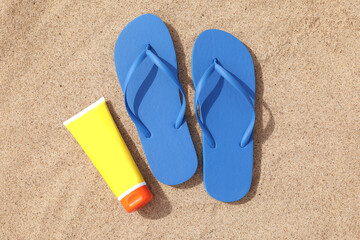 Fototapeta na wymiar Blue flip flops and sunscreen on sand, flat lay