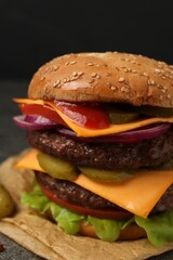 Delicious burger with meat cutlets, cheese, pickled cucumbers and lettuce on grey table, closeup