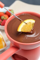 Dipping fresh orange into fondue pot with melted chocolate at table, closeup