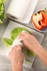 Woman wiping lettuce with paper towels at grey table, top view