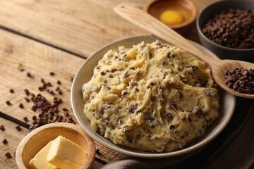 Chocolate chip cookie dough in bowl and ingredients on white wooden table, closeup