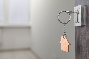 Mortgage and real estate. Open door with key and house shaped keychain against blurred background, space for text