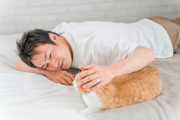 家のベッドルーム・寝室でくつろぐ猫と飼い主の男性（リラックス）
