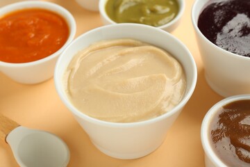 Bowls with healthy baby food and spoon on pale orange background, closeup