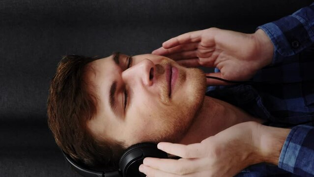 Portrait of man putting on headphones and listening to music. Vertical video