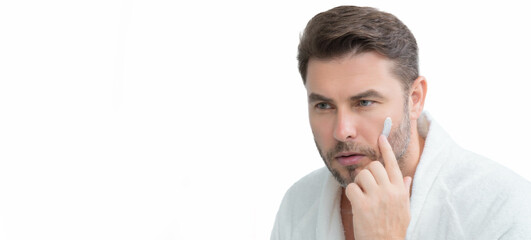 Fototapeta premium Close up portrait of man 40s applying cream on face. White isolated banner with copy space. Portrait of beauty man with cosmetic cream on skin. Facial treatment. male beauty.