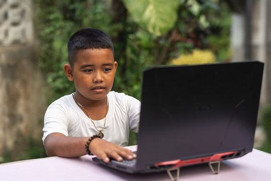 A young tech savvy rural asian boy typing on a laptop. Outdoor scene at the garden.