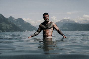 Muscular Hispanic man splashing water in lake. Attractive male sexy model in water. Handsome boy rest in Alps lake water. Sexy man naked torso in water. Man freedom lifestyle. Strong muscles guy.