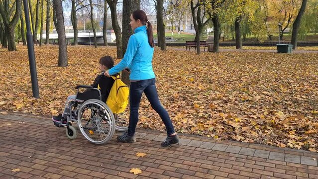 Mom with her little disabled daughter in wheelchair in park. Happy mother and child hugging and love in family