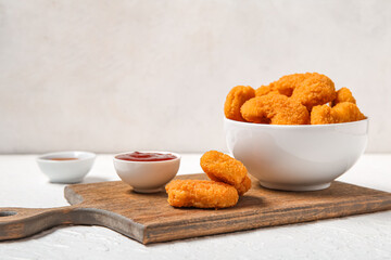 Wooden board with bowl of tasty nuggets and ketchup on white background