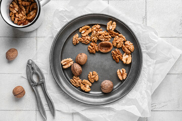 Plate and cup of tasty walnuts on white tile background