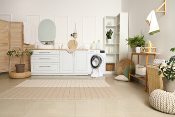 Interior of stylish laundry room with washing machine, houseplants and cleaning supplies - obrazy, fototapety, plakaty