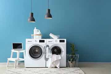 Interior of modern laundry room with washing machines and laptop near blue wall