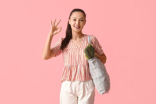 Young Asian woman with eco bag full of fresh food showing OK gesture on pink background
