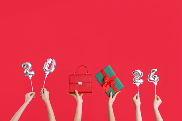 Many hands with Christmas gift, bag and 2024 balloons on red background