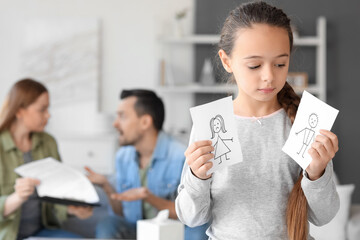 Sad little girl with torn drawing of family at home. Divorce concept