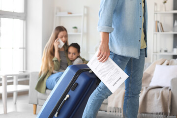Young man with divorce decree and suitcase leaving his family at home - obrazy, fototapety, plakaty