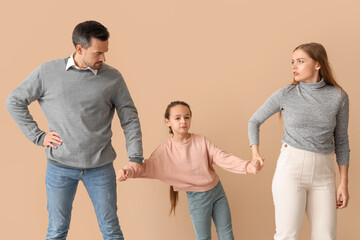 Sad little girl with her divorced parents on beige background