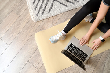 Sporty young woman using laptop on fitness mat at home, top view