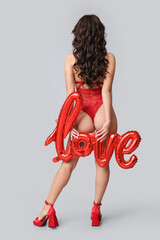Beautiful young Asian woman with balloon in shape of word LOVE wearing sexy underwear on grey background, back view
