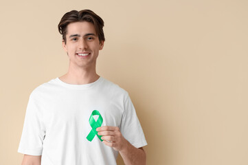 Young man with green ribbon on beige background. Glaucoma awareness month