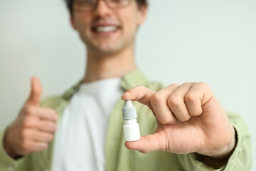 Young man with eye drops showing thumb-up on light background, closeup. Glaucoma awareness month