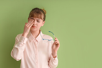 Tired young businesswoman with eyeglasses on green background. Glaucoma awareness month