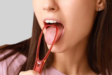 Young woman with tongue scraper on grey background - obrazy, fototapety, plakaty