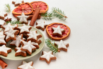 Plate with delicious stars shaped Christmas cookies, orange dried pieces and fir tree branches on light background, closeup