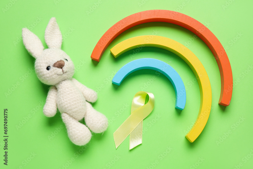 Wall mural Golden ribbon with toys on green background. Childhood cancer awareness concept