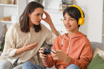Teenage boy playing video game and his upset mother at home. Family problem concept