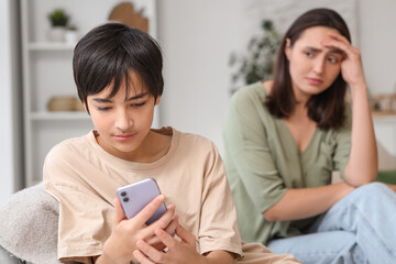 Teenage boy using mobile phone and his upset mother at home. Family problem concept