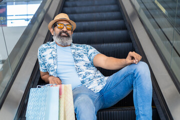 Senior indian man wearing hat and sunglasses sitting on escalator stairs and riding escalator in...