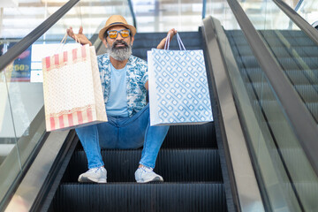 Senior indian man wearing hat and sunglasses sitting on escalator stairs and riding escalator in...