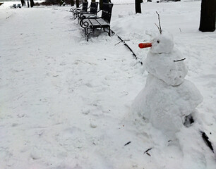 Winter view with a snowman in a public park. Fun homemade snow sculpture.