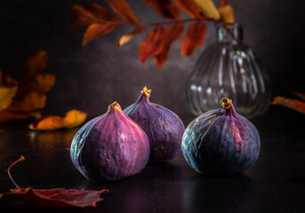 Fresh figs and autumn leaves lie on a dark wooden table. Beautiful large blue fig fruits.