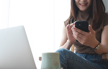 Smiling asian business woman in casual wear using mobile phone while working on laptop at coffee shop. Young woman freelancer online working and using smartphone