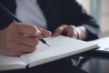 Close up of woman's hands writing on paper notebook during working on laptop computer, taking note and work planning at modern office, e-learning, online studying