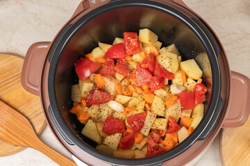 Modern, bright light multi cooker with raw products. Cooking stewed potatoes with meat in multicooker. Top view of multi cooker with prepared vegetables, spices and herbs.