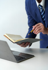 businessman working on laptop computer Print email check work Send information online on white desk Hold a notebook and use a pen to point to business goals that plan success in the office.