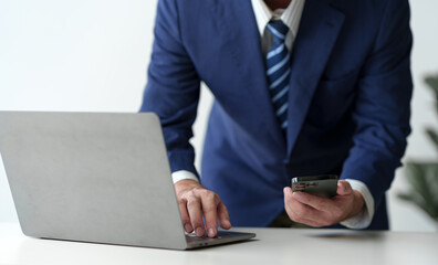 Businessman holds smartphone, checks email, checks job details on Laptop computer on white desk to point to successful business goals in office.