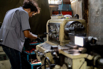 Fototapeta premium Asian worker in production plant drilling at machine. Professional worker near drilling machine on factory. finishing metal working internal steel surface on lathe grinder machine with flying sparks.