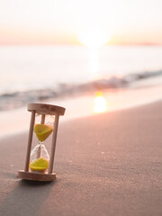 Hourglass on the beach in the sunset time. The concept about countdown to Summer, Travel, Vacation and Relaxation.