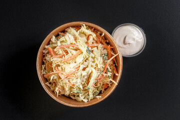 Vitamin salad with fresh cabbage in paper take away container with sauce on black background.