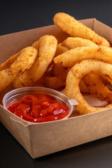 Golden crispy onion rings coated with breadcrumbs and deep fried. Fried onion rings in a paper box.