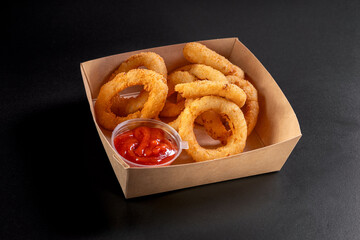 Golden crispy onion rings coated with breadcrumbs and deep fried. Fried onion rings in a paper box.