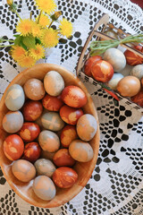 Easter eggs on a wooden plate, spring dandelion flowers decoration on a table, and traditional natural leaf-based decoration on colored eggs 