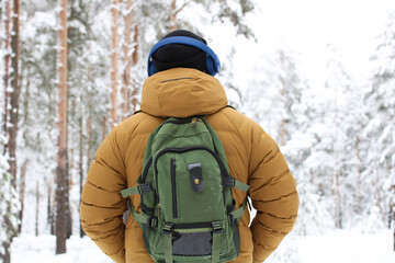young man wearing headphones walks in a snowy forest. guy enjoys the winter nature in the park.